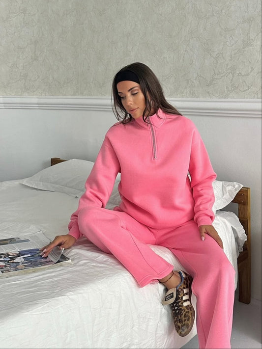 Person wearing a pink tracksuit sitting on a bed with a magazine.